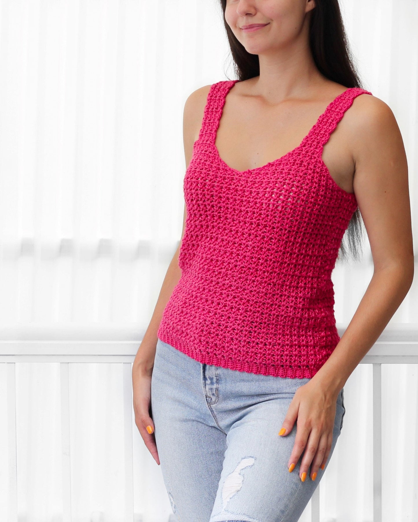 May include: A pink crocheted tank top with a v-neck and thin straps. The top is made with a simple stitch pattern and has a relaxed fit.