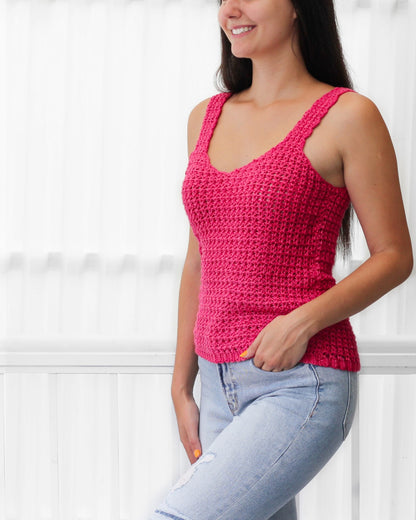 May include: A pink crochet tank top with a v-neck and thin straps. The tank top is worn with light blue jeans.