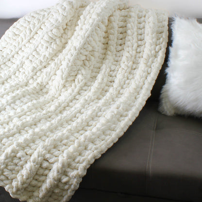 May include: A white chunky knit throw blanket with a soft, fluffy texture. The blanket is draped over a gray couch.