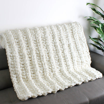 May include: A white knitted throw blanket with a chunky cable knit pattern. The blanket is draped over a gray couch.