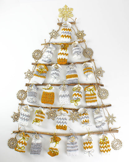 May include: A Christmas advent calendar made of crocheted pouches in white and mustard yellow hanging from branches in the shape of a tree. The pouches are numbered 1 through 24 and decorated with wooden snowflakes.