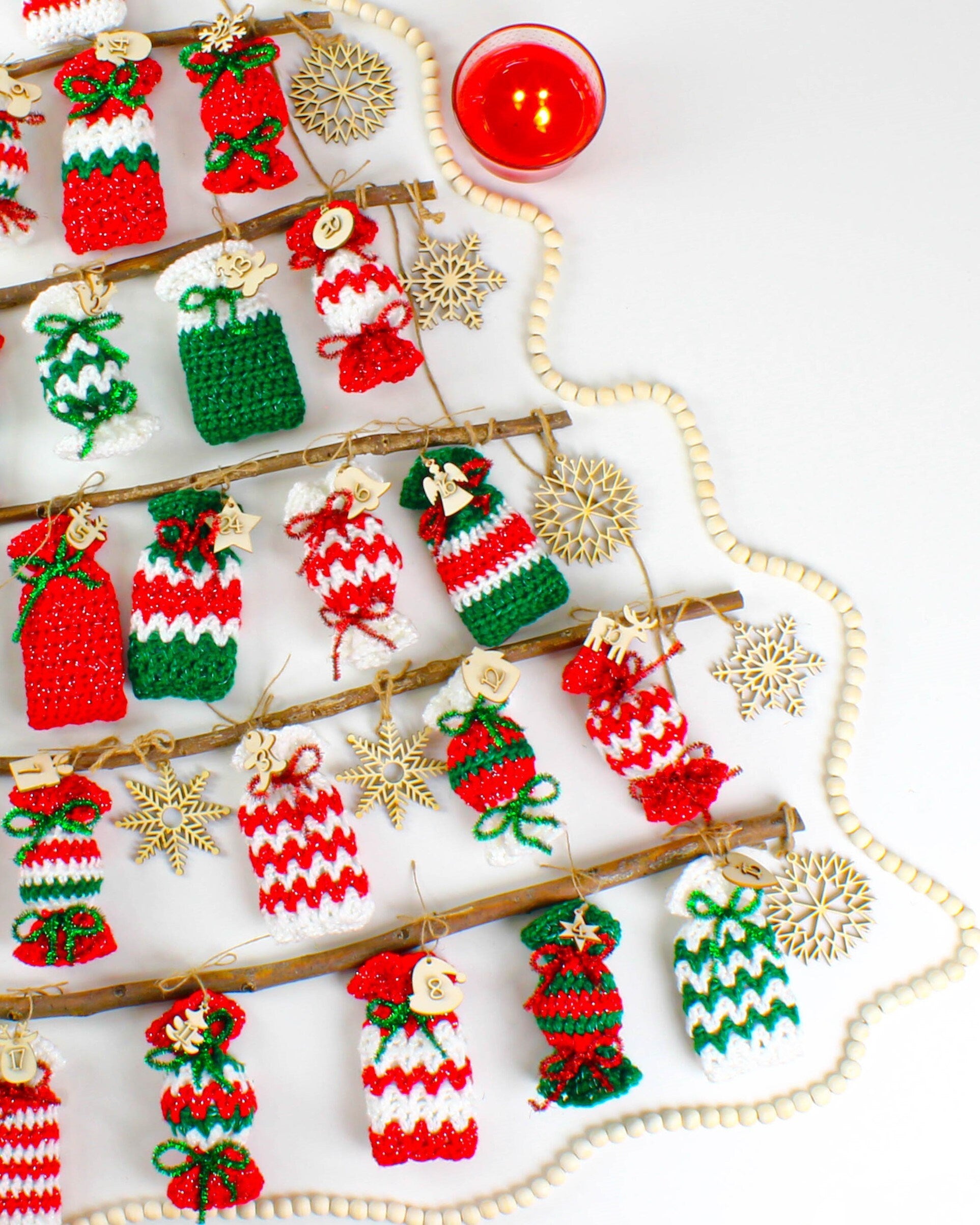 May include: A Christmas advent calendar made of crocheted candy cane ornaments hanging from wooden branches. The ornaments are red, white, and green with glitter and are numbered 1 through 24. The calendar is decorated with wooden snowflakes and a string of white beads.