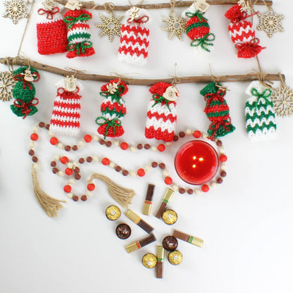 May include: A white surface with a red candle, a string of brown and red beads, and 12 crocheted candy cane ornaments in red, white, and green. There are also 12 small chocolate candies.