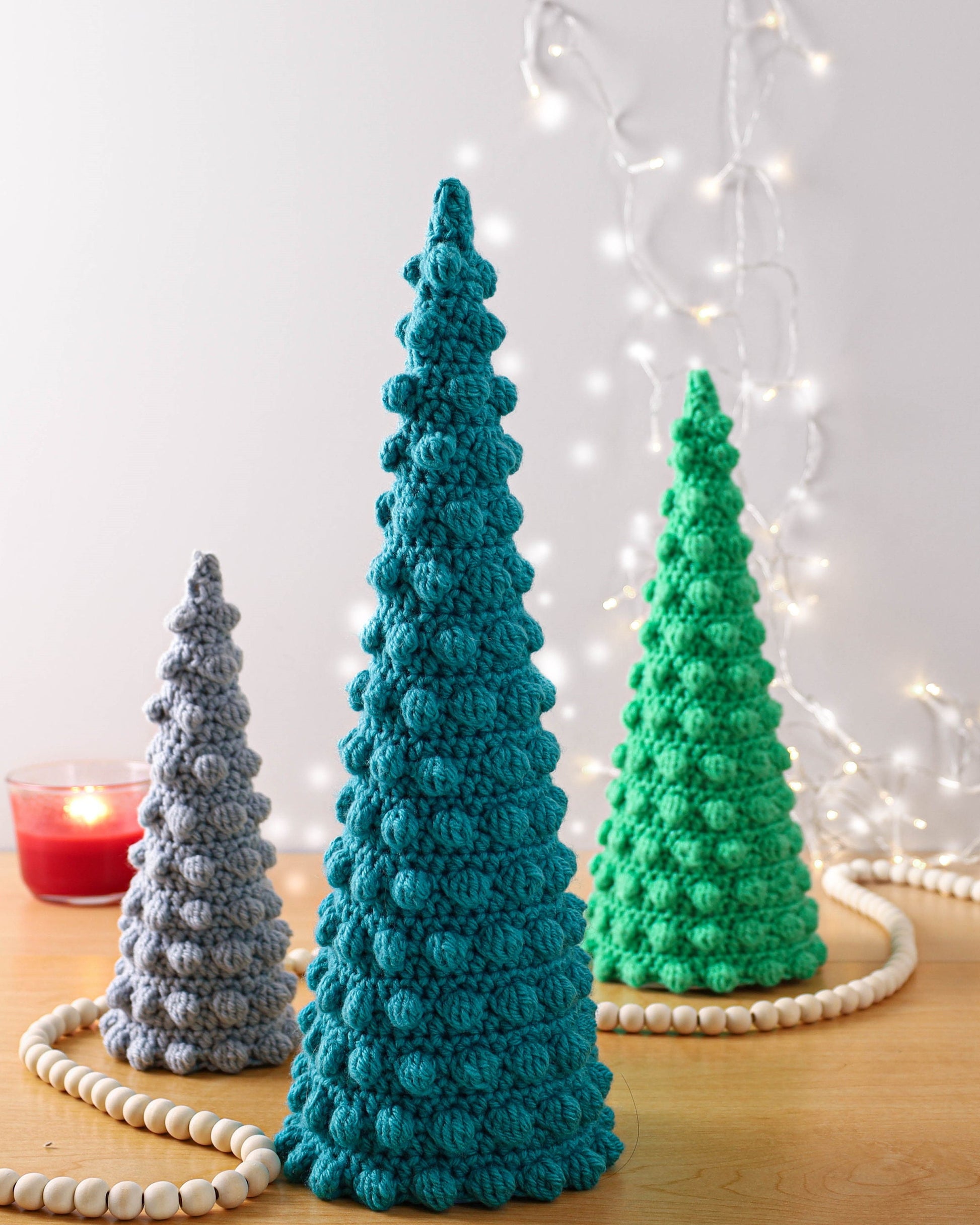 May include: Three crocheted Christmas trees in different sizes. The largest tree is teal, the medium tree is green, and the smallest tree is gray.