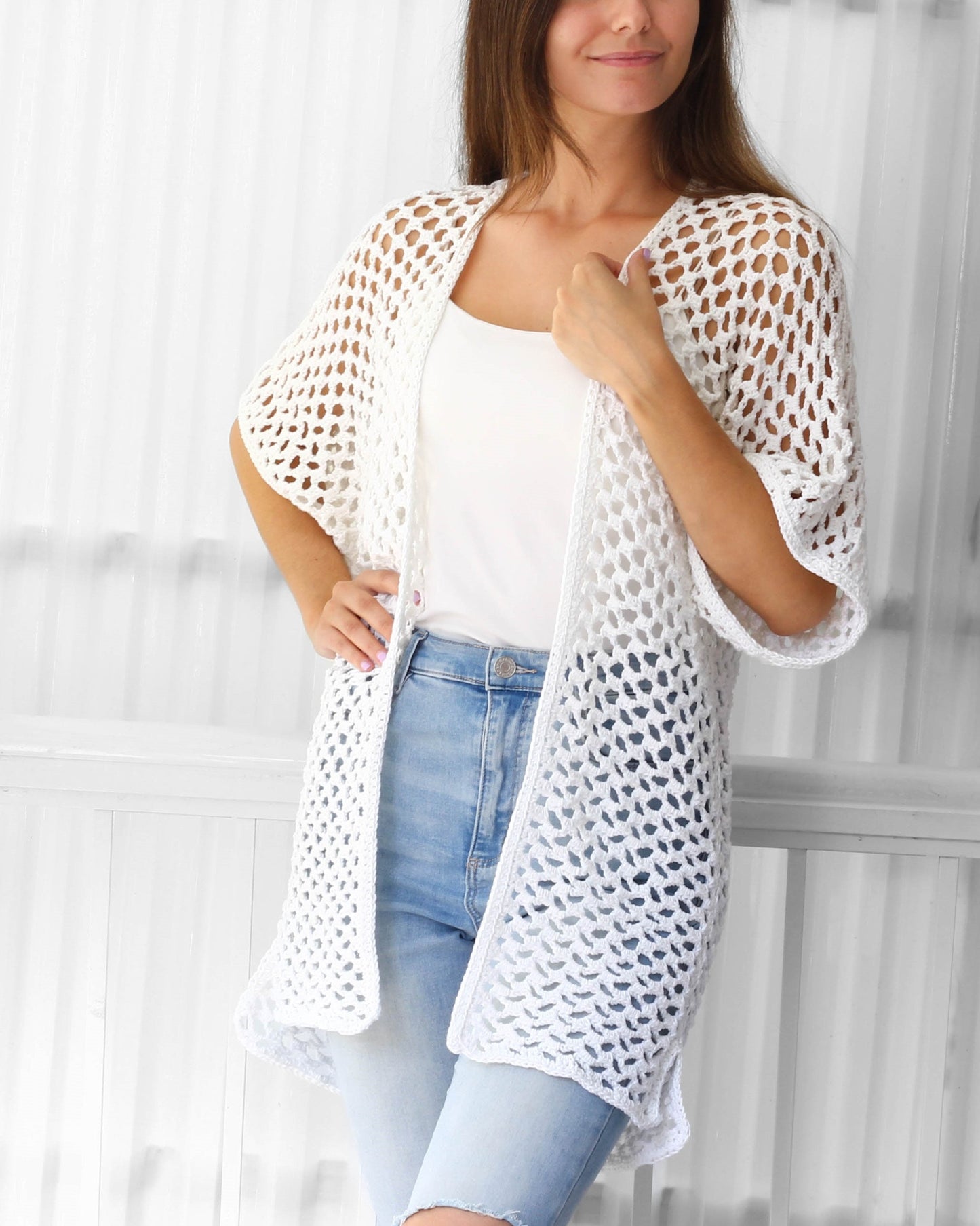 May include: White crochet cardigan with a loose fit and a delicate openwork pattern. The cardigan has a long, flowing silhouette and short sleeves.