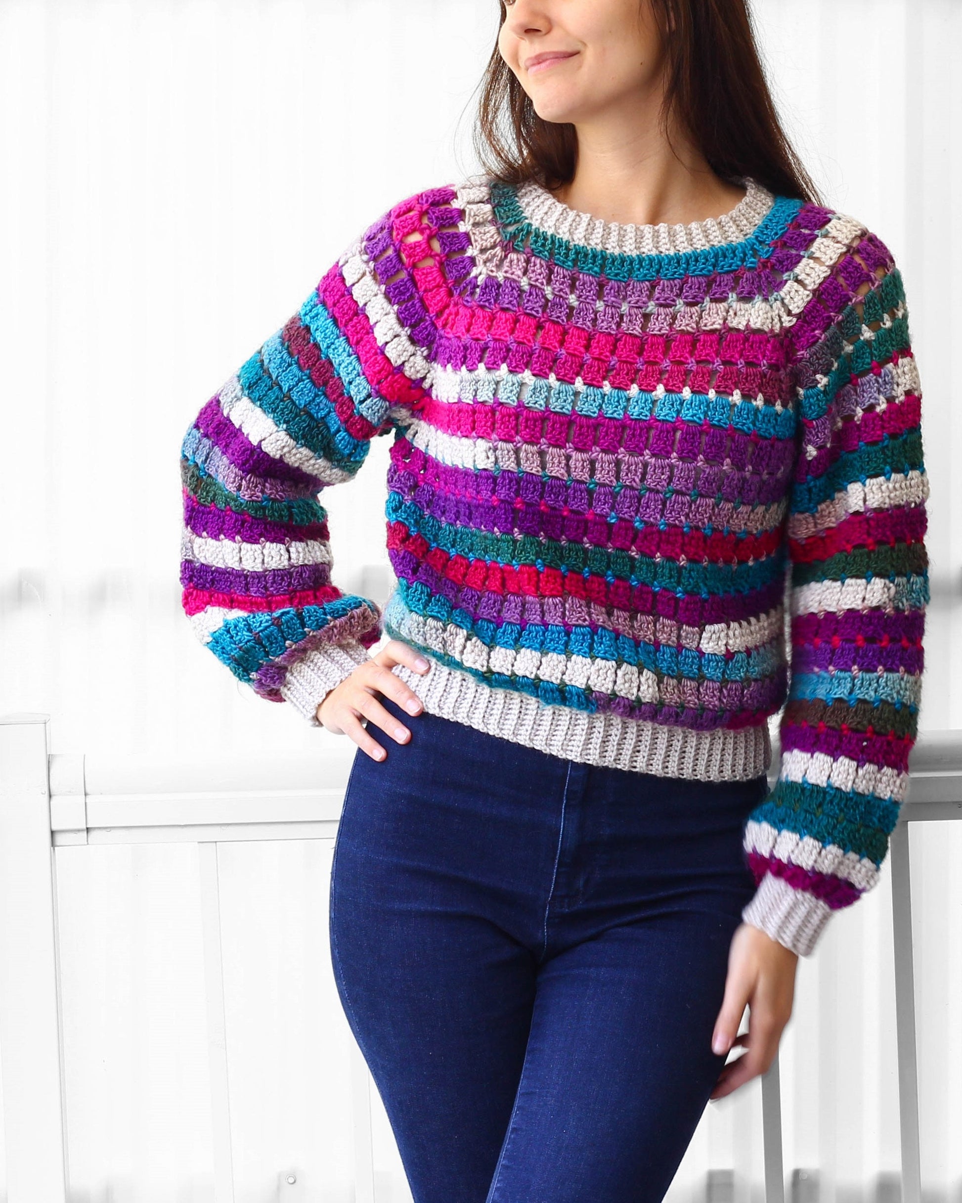 May include: A colorful striped crochet sweater with a loose fit and long sleeves. The sweater is made with a variety of colors, including pink, purple, blue, green, and white.