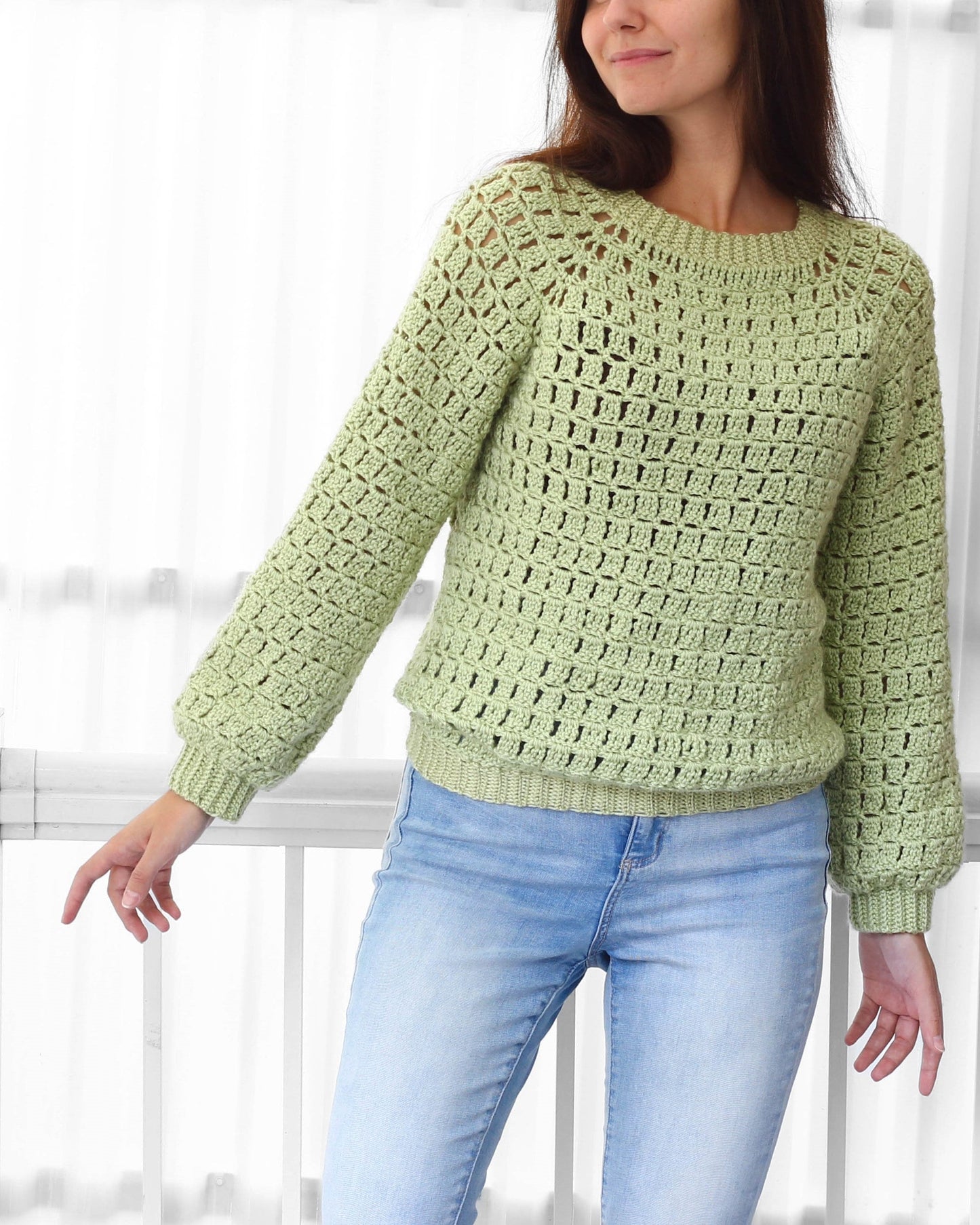 May include: A light green crocheted sweater with a loose fit and long sleeves. The sweater has a square stitch pattern and a round neckline.