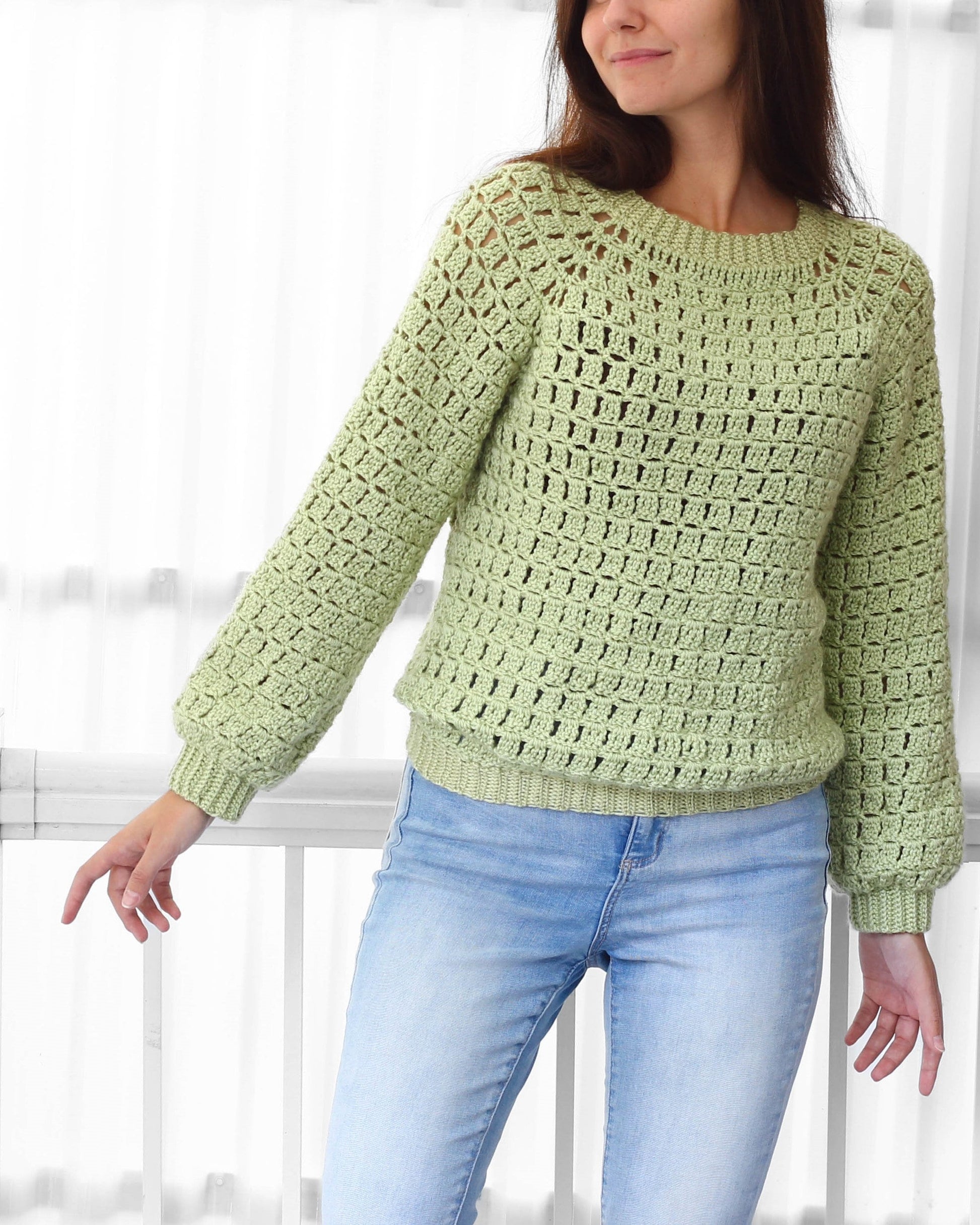 May include: A light green crocheted sweater with a loose fit and long sleeves. The sweater has a square stitch pattern and a round neckline.