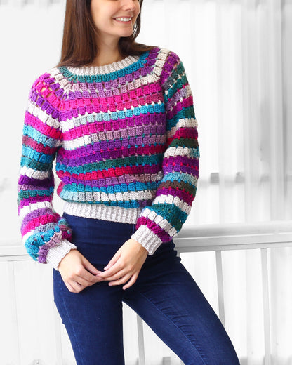 May include: A colorful striped crochet sweater with long sleeves and a round neckline. The sweater is made with a variety of colors, including pink, purple, blue, green, and brown.