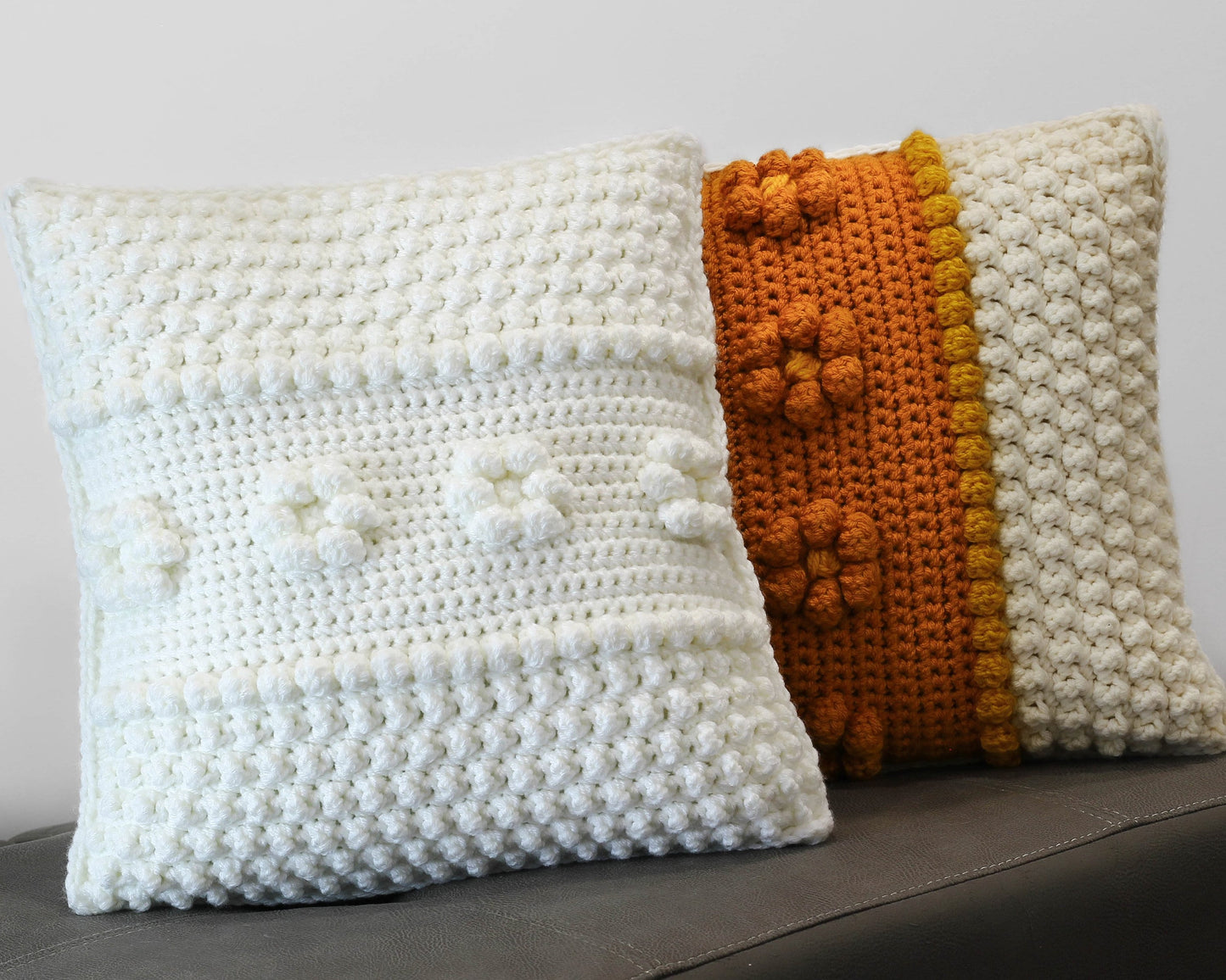 May include: Two crocheted throw pillows, one white with a textured pattern and the other with a white and orange striped pattern.