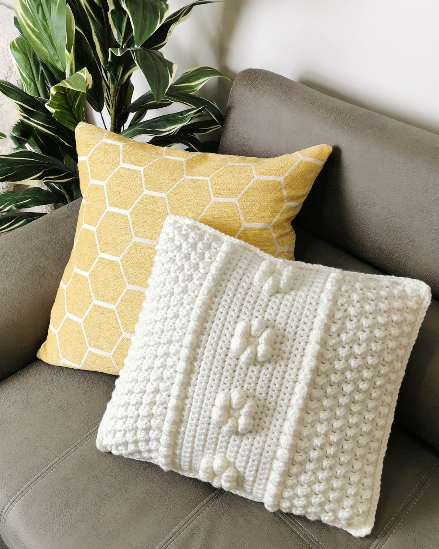 May include: Two throw pillows on a gray couch. One pillow is yellow with a honeycomb pattern and the other is white with a textured design.