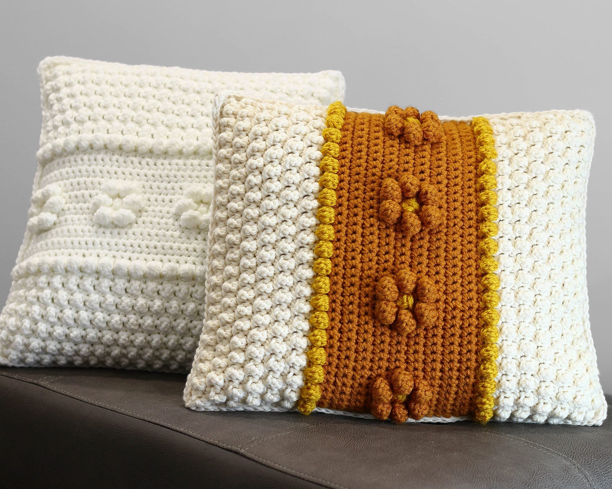May include: Two crocheted throw pillows, one white with a textured surface and the other white with a yellow and brown stripe and textured surface.
