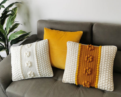 May include: Three crocheted throw pillows on a gray couch. The pillows are white with a textured pattern and a yellow stripe with a textured pattern.