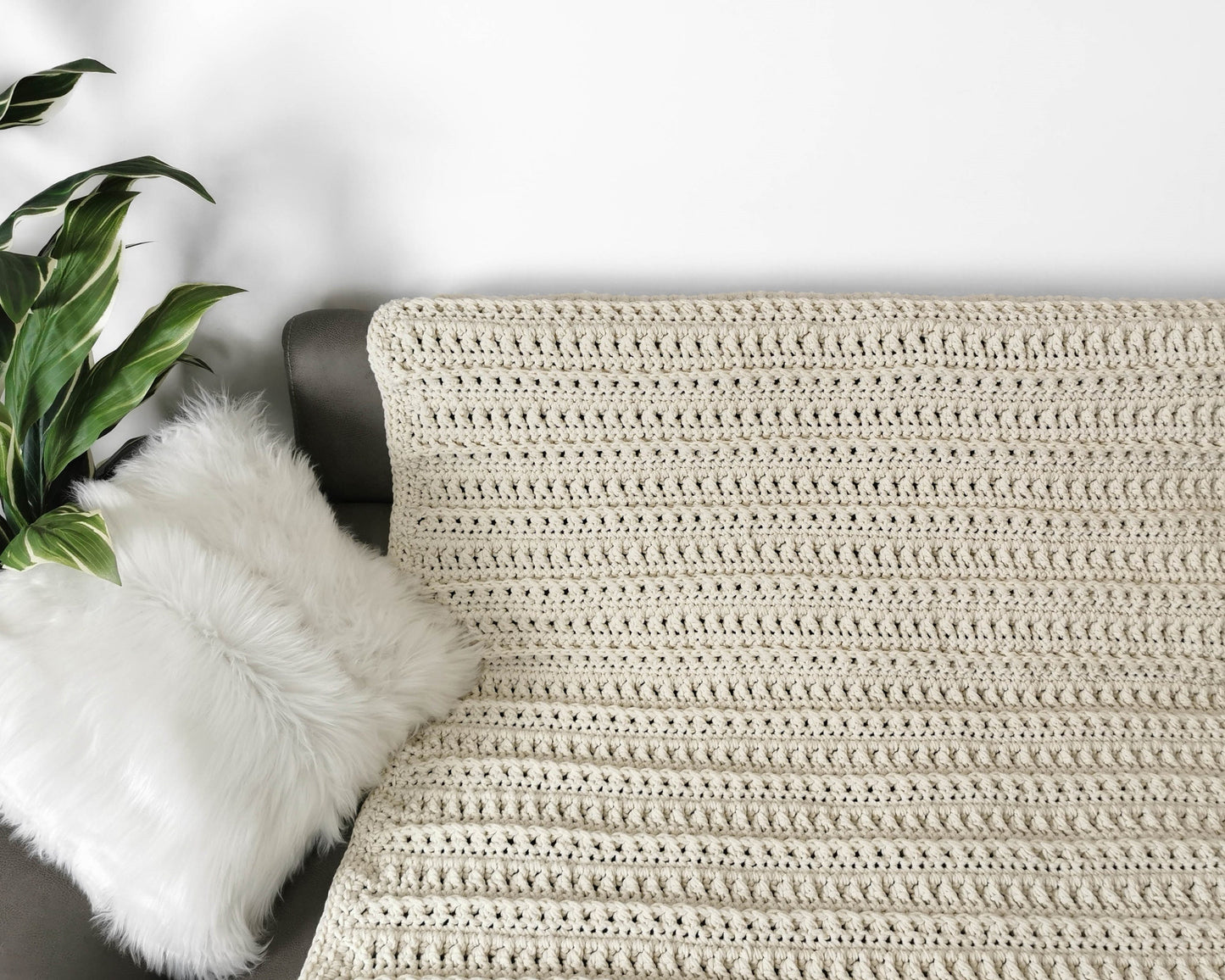 May include: A cream-colored crocheted throw blanket with a textured pattern, draped over a couch with a white faux fur pillow.