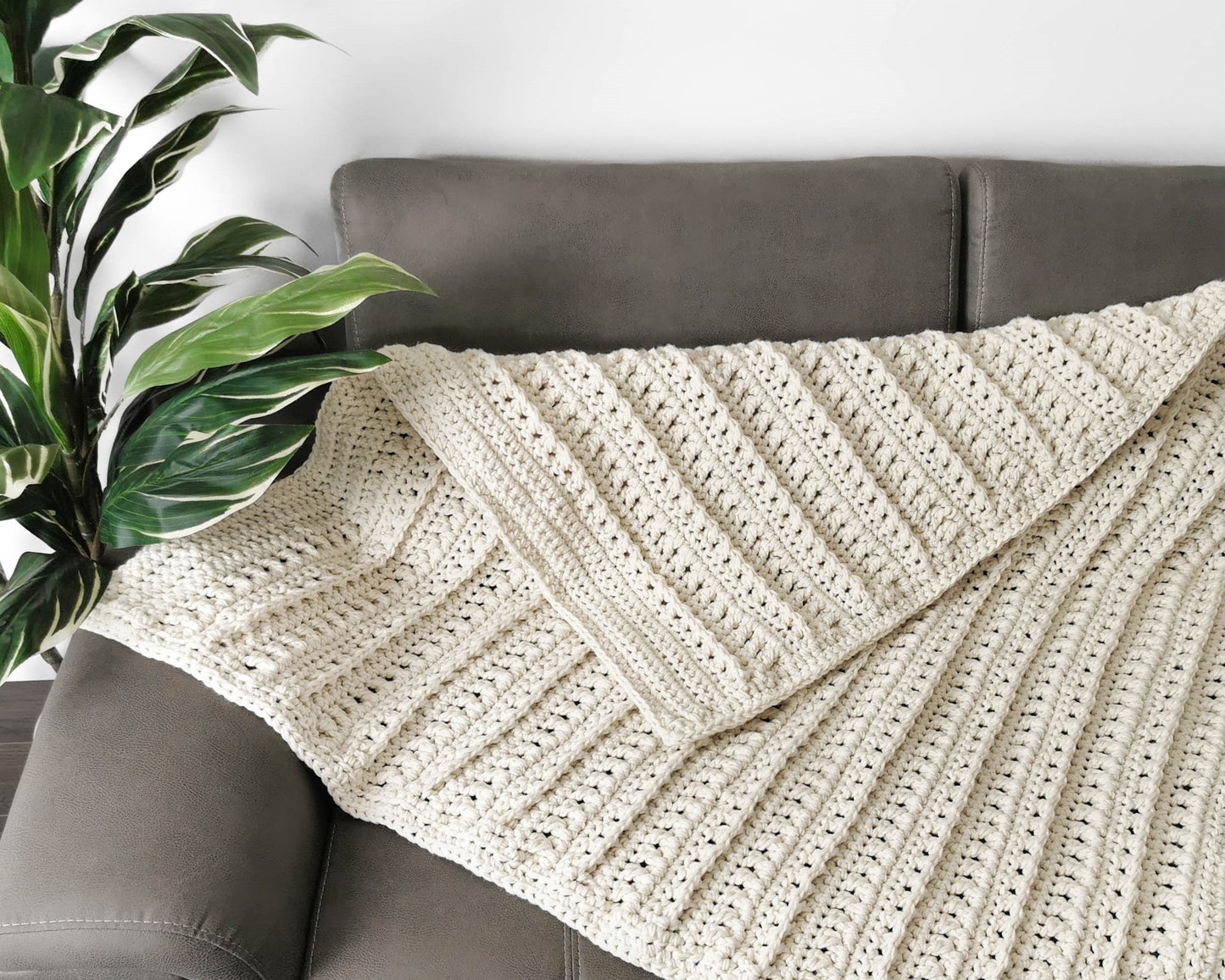 May include: A cream-colored crocheted throw blanket with a textured stitch pattern is draped over a gray couch.