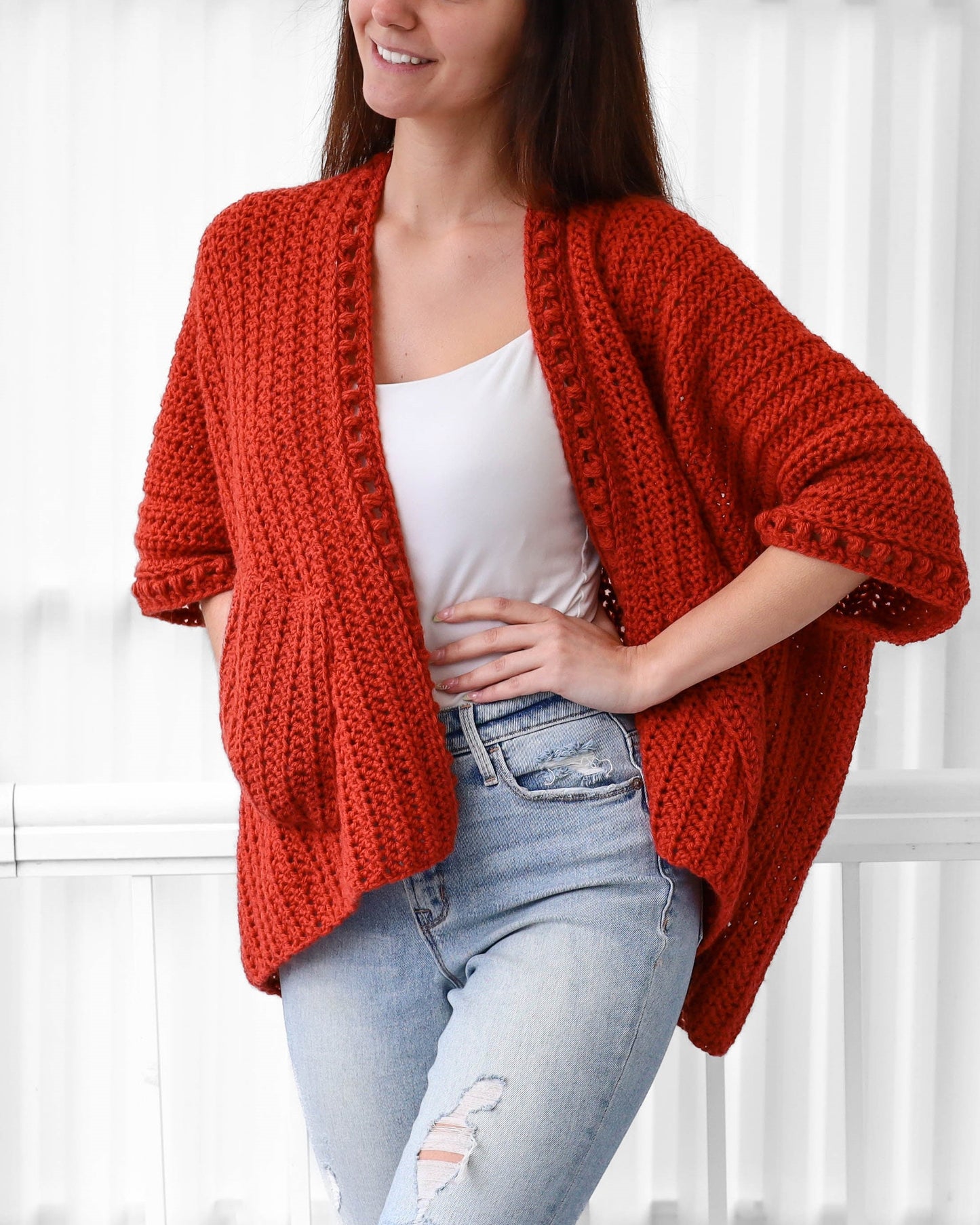 May include: A red crocheted cardigan with a loose fit and pockets. The cardigan has a V-neck and is made with a textured stitch.