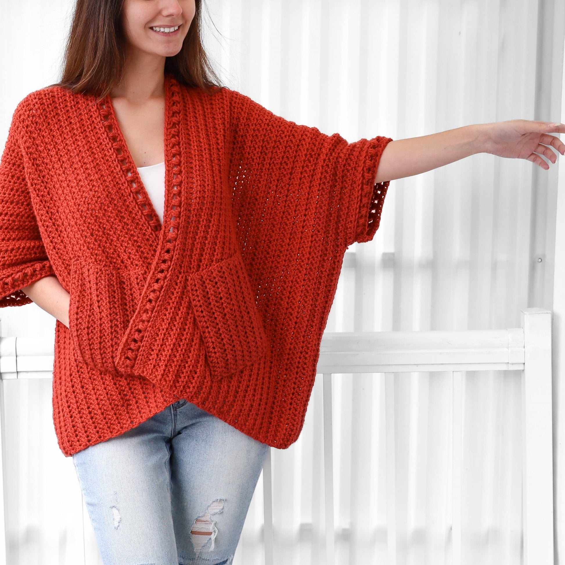 May include: A red crocheted cardigan with a V-neck and pockets. The cardigan has a crocheted trim around the neckline and sleeves.