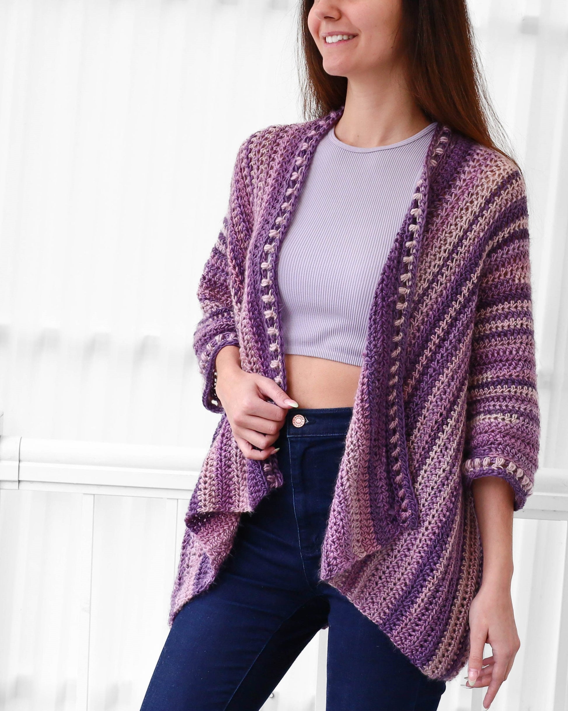 May include: A purple and pink striped crochet cardigan with a slightly open front and a slightly flared hem. The cardigan has a crocheted border with small beads.