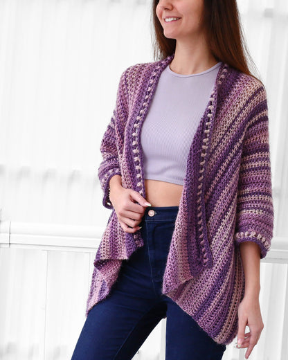 May include: A purple and pink striped crochet cardigan with a slightly open front and a slightly flared hem. The cardigan has a crocheted border with small beads.