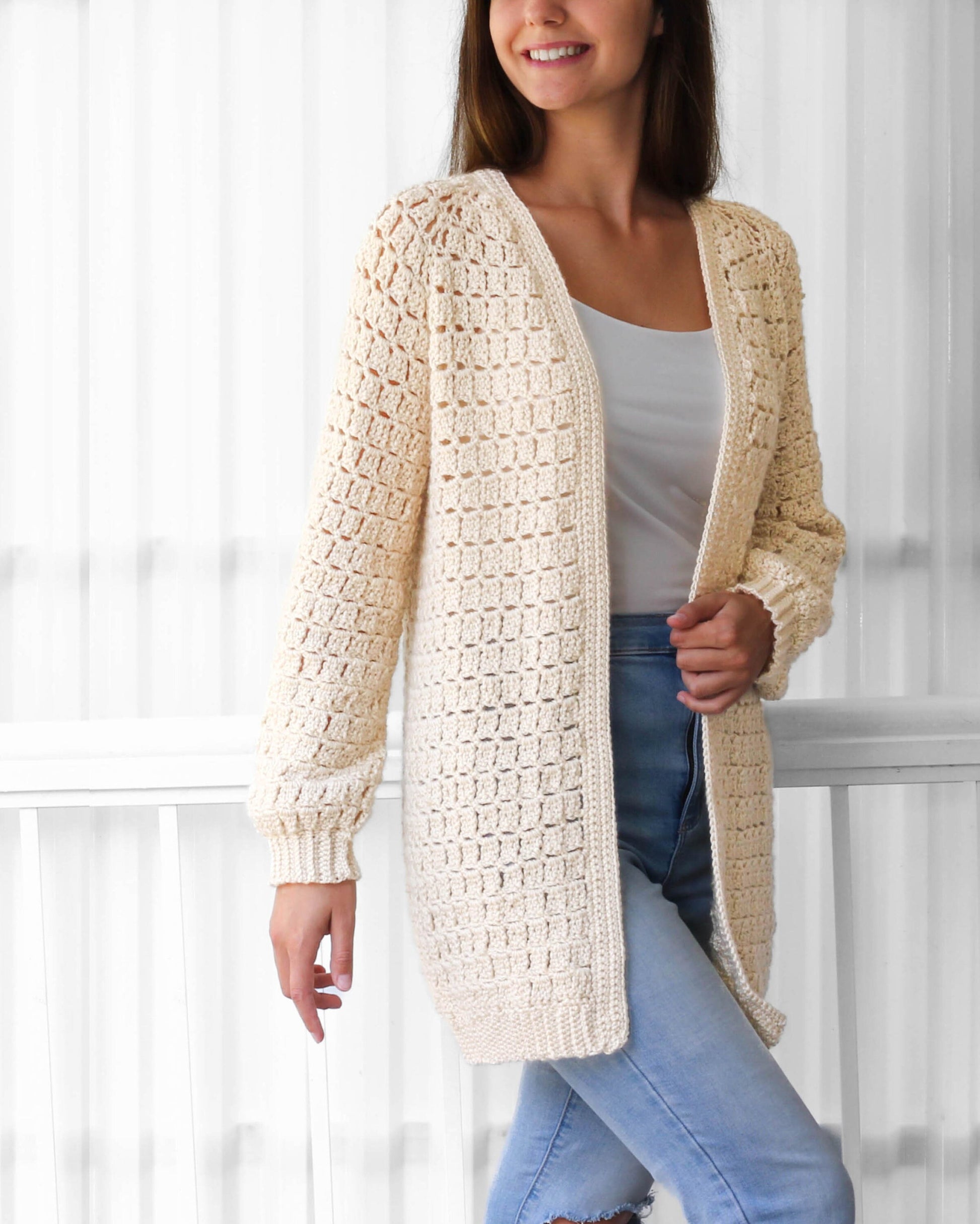 May include: A cream-colored crocheted cardigan with a long, open front and long sleeves. The cardigan is made with a delicate stitch pattern and has a relaxed fit.