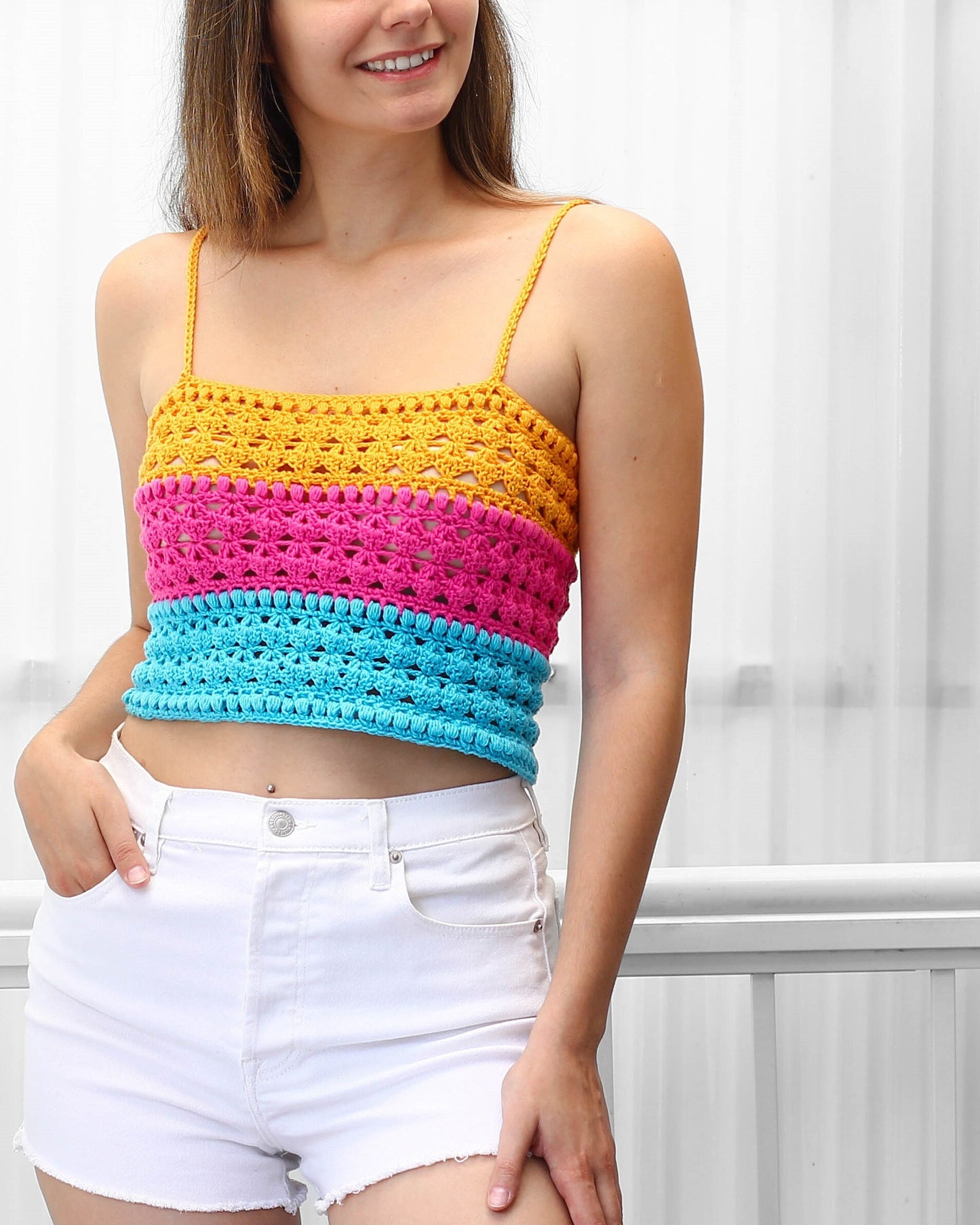 May include: A colorful crochet top with yellow, pink, and blue stripes. The top has a square neckline and thin straps.