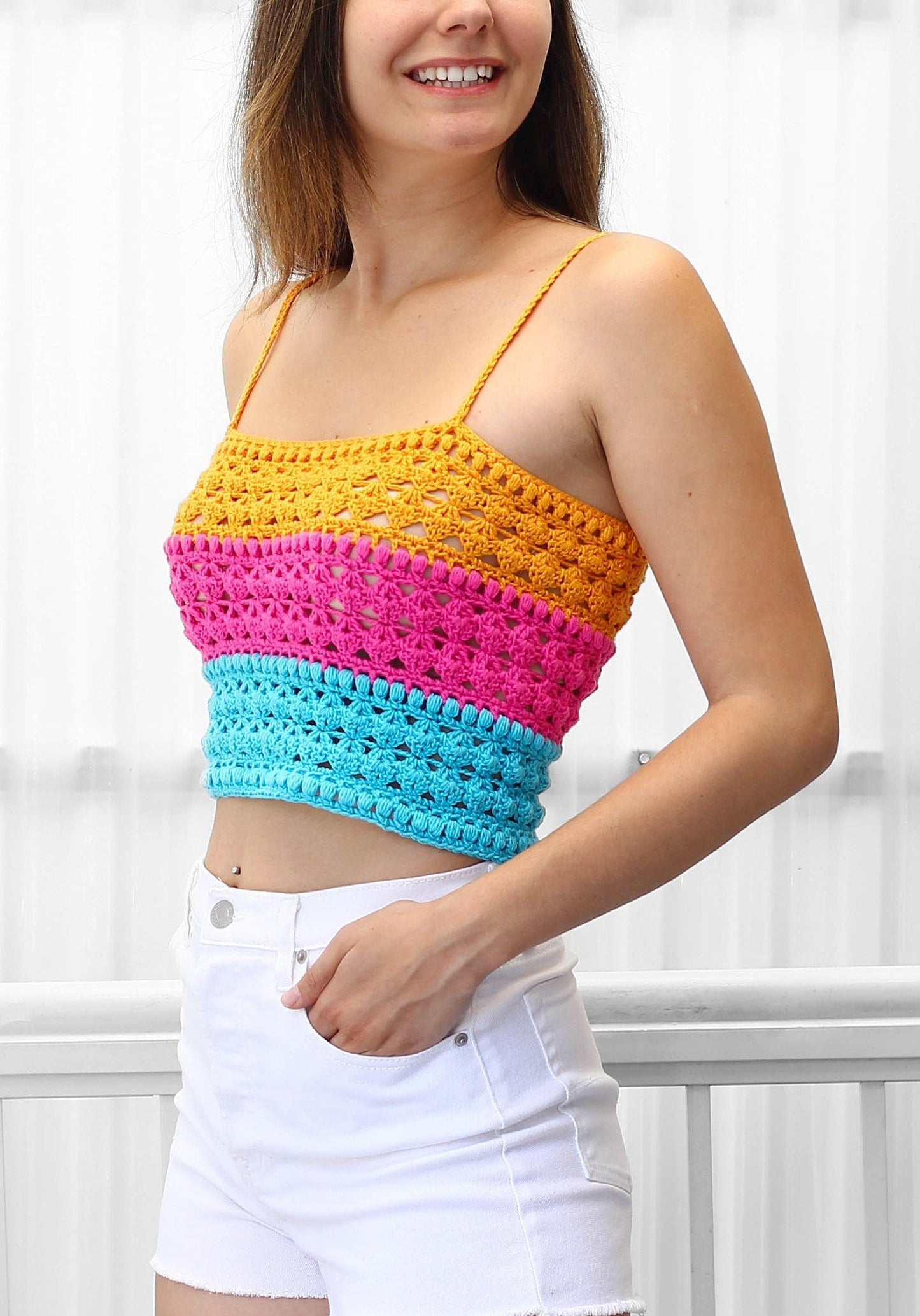 May include: A colorful crochet top with a yellow, pink, and blue striped pattern. The top is sleeveless and has a cropped length.