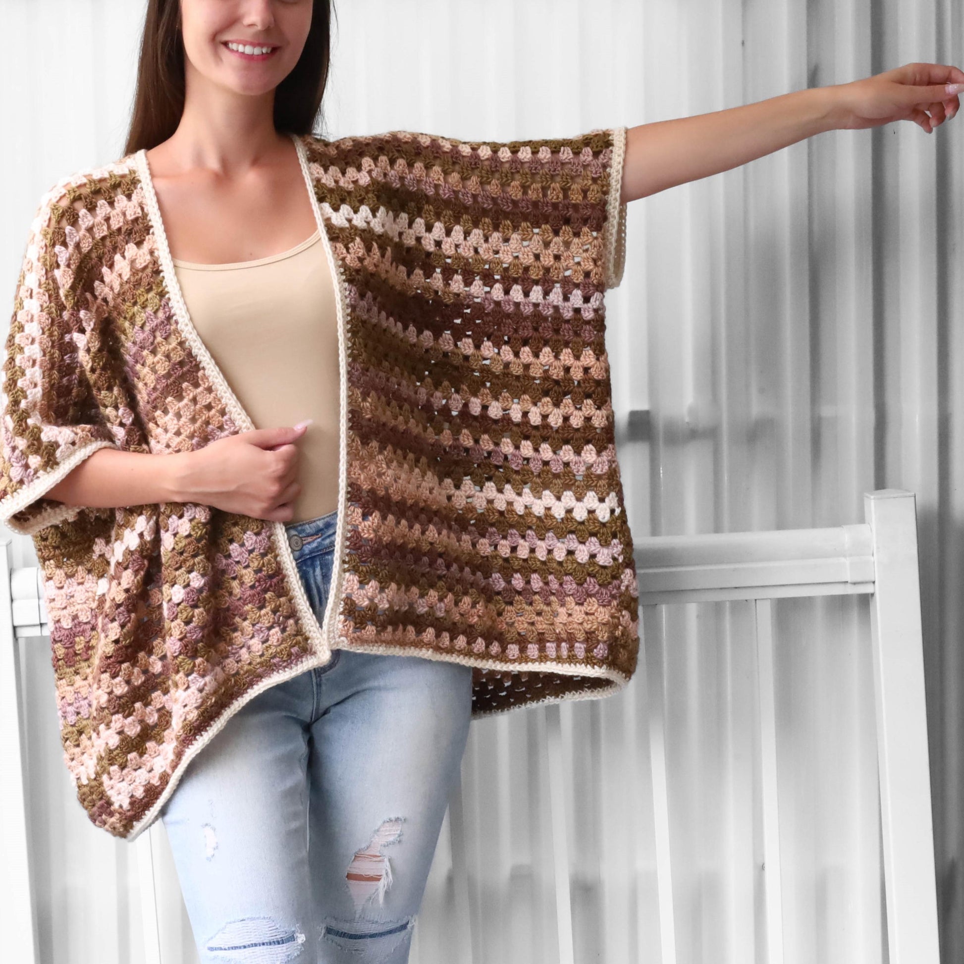 May include: A brown, pink, and white striped crochet cardigan with a white trim. The cardigan is open in the front and has a relaxed fit.