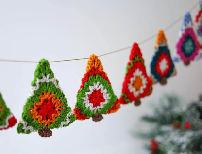 May include: A garland of crocheted Christmas trees in green, red, orange, white, and blue. The trees are strung together with twine and hang from a white wall.