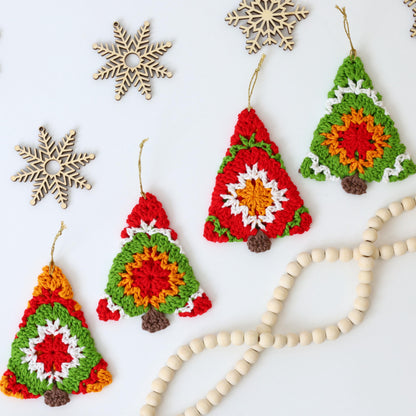 May include: Four crocheted Christmas tree ornaments in red, green, white, and orange with a brown felt base. The ornaments are hanging from white string and are displayed on a white surface with wooden snowflakes and a string of wooden beads.
