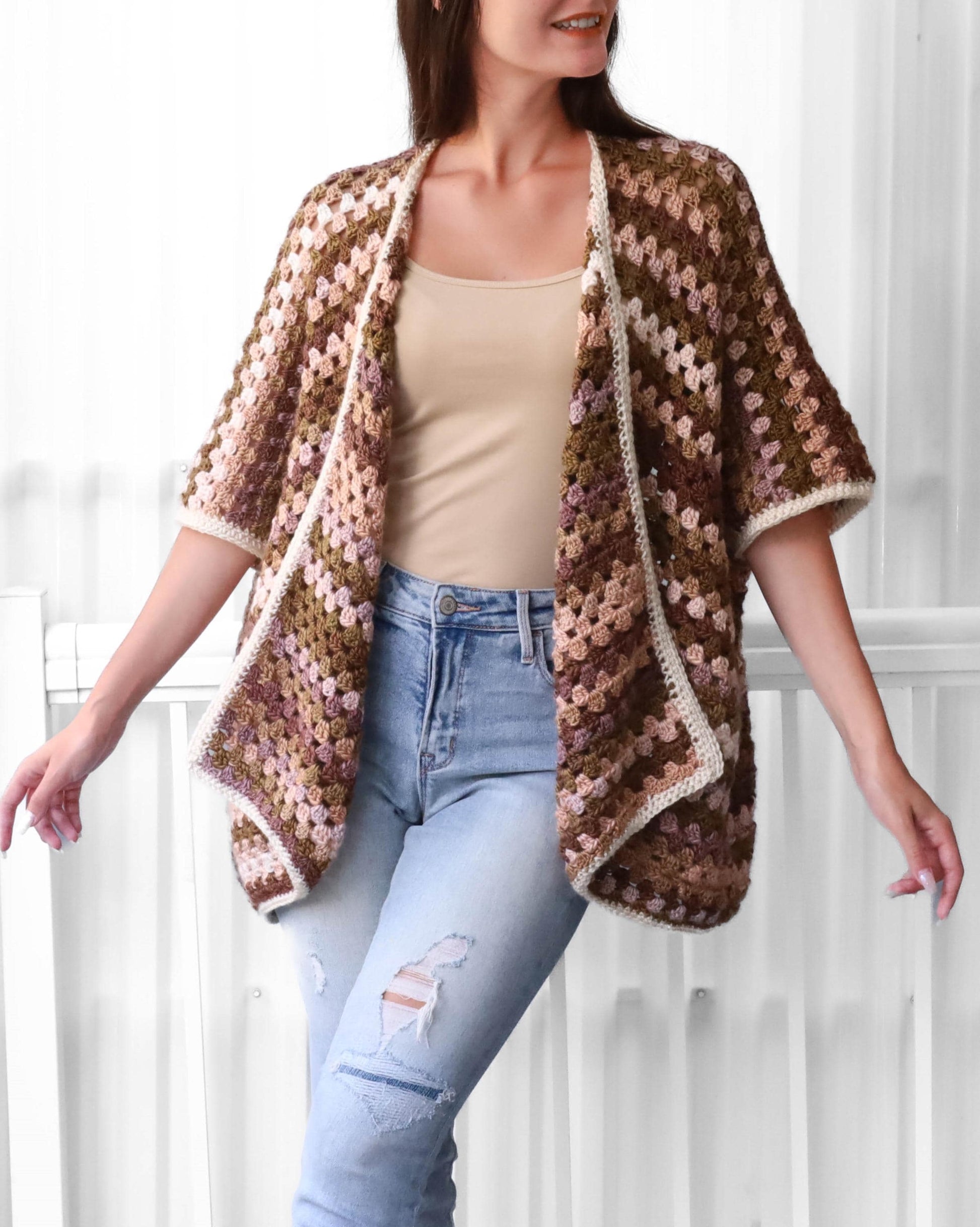 May include: A brown, pink, and white crocheted cardigan with a granny square pattern. The cardigan has a loose fit and short sleeves.
