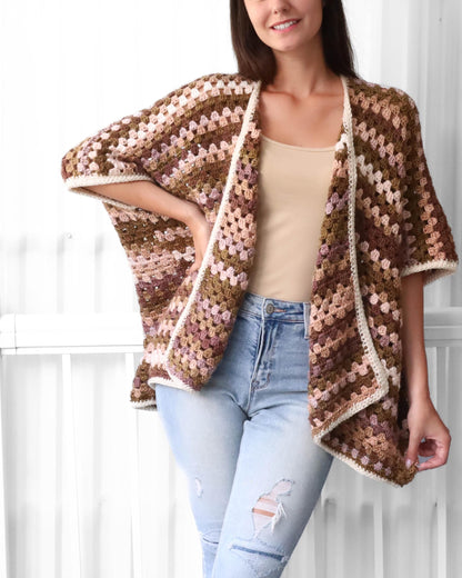 May include: A brown, pink, and white crocheted cardigan with a slightly asymmetrical hemline. The cardigan has a loose fit and short sleeves.