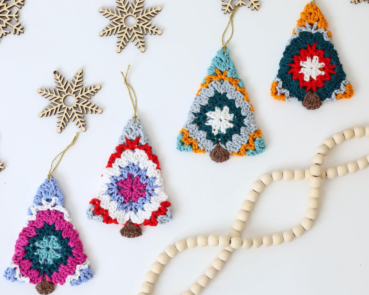 May include: Five crocheted Christmas tree ornaments in various colors, including red, blue, green, white, and yellow. The ornaments are hanging from white string and are on a white background.