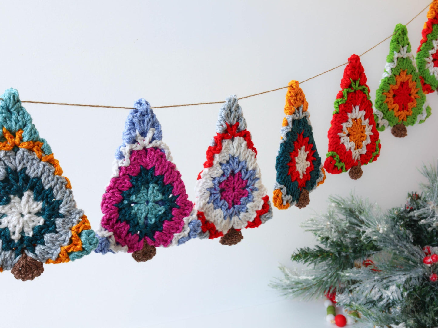 May include: A colorful crocheted Christmas tree garland with red, green, blue, white, and orange accents. The garland is strung on a twine string and is perfect for decorating a home for the holidays.