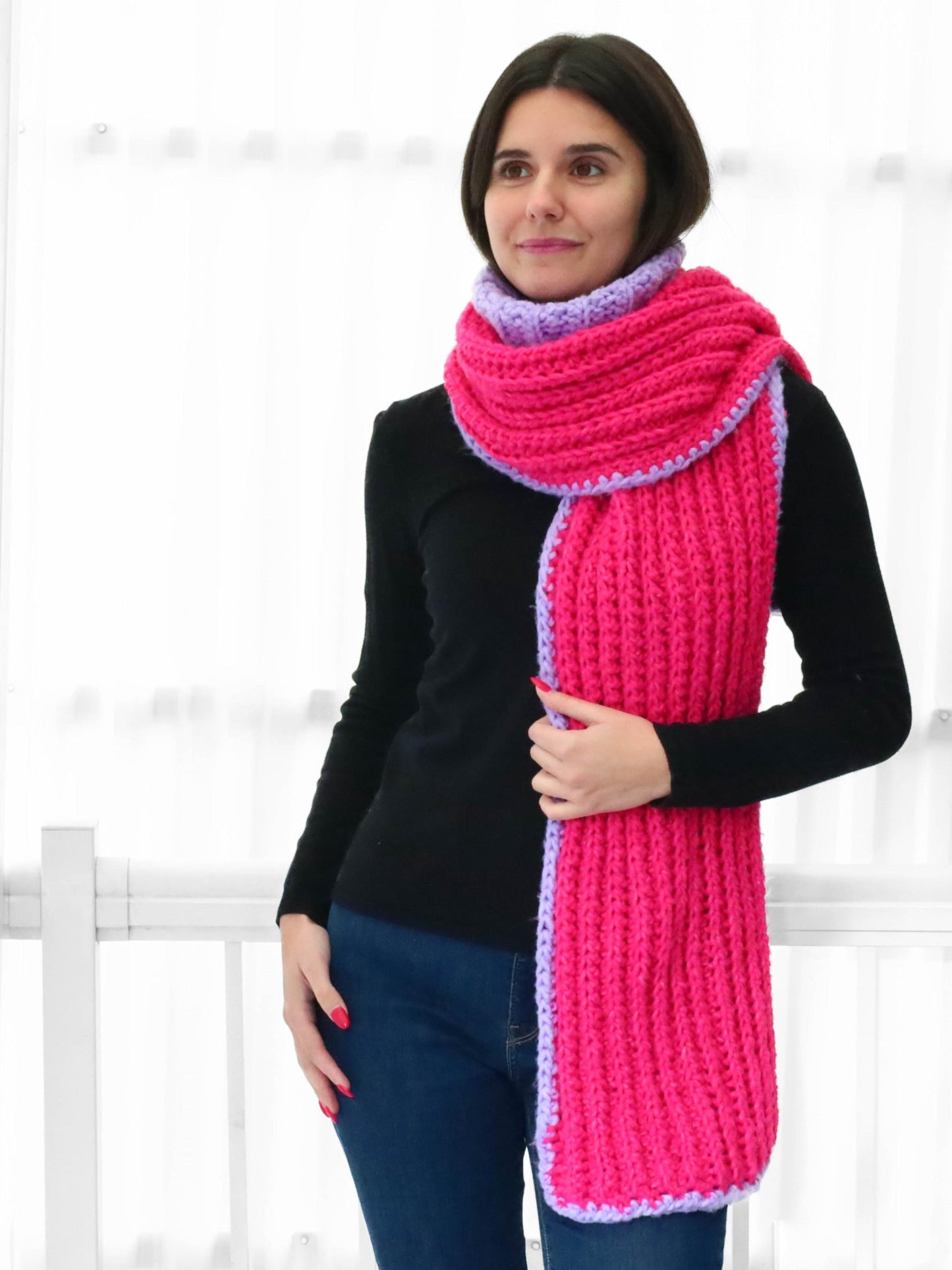 May include: A pink and purple knitted scarf with a ribbed texture. The scarf is long and wide, and it is folded in half.