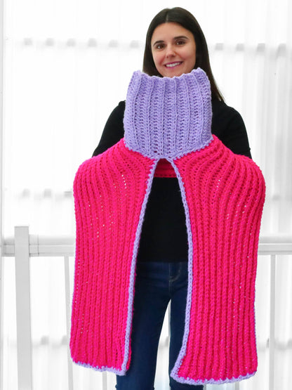 May include: A pink and purple crocheted cowl with a high neck and long sleeves. The cowl is made with a textured stitch and has a split in the back.