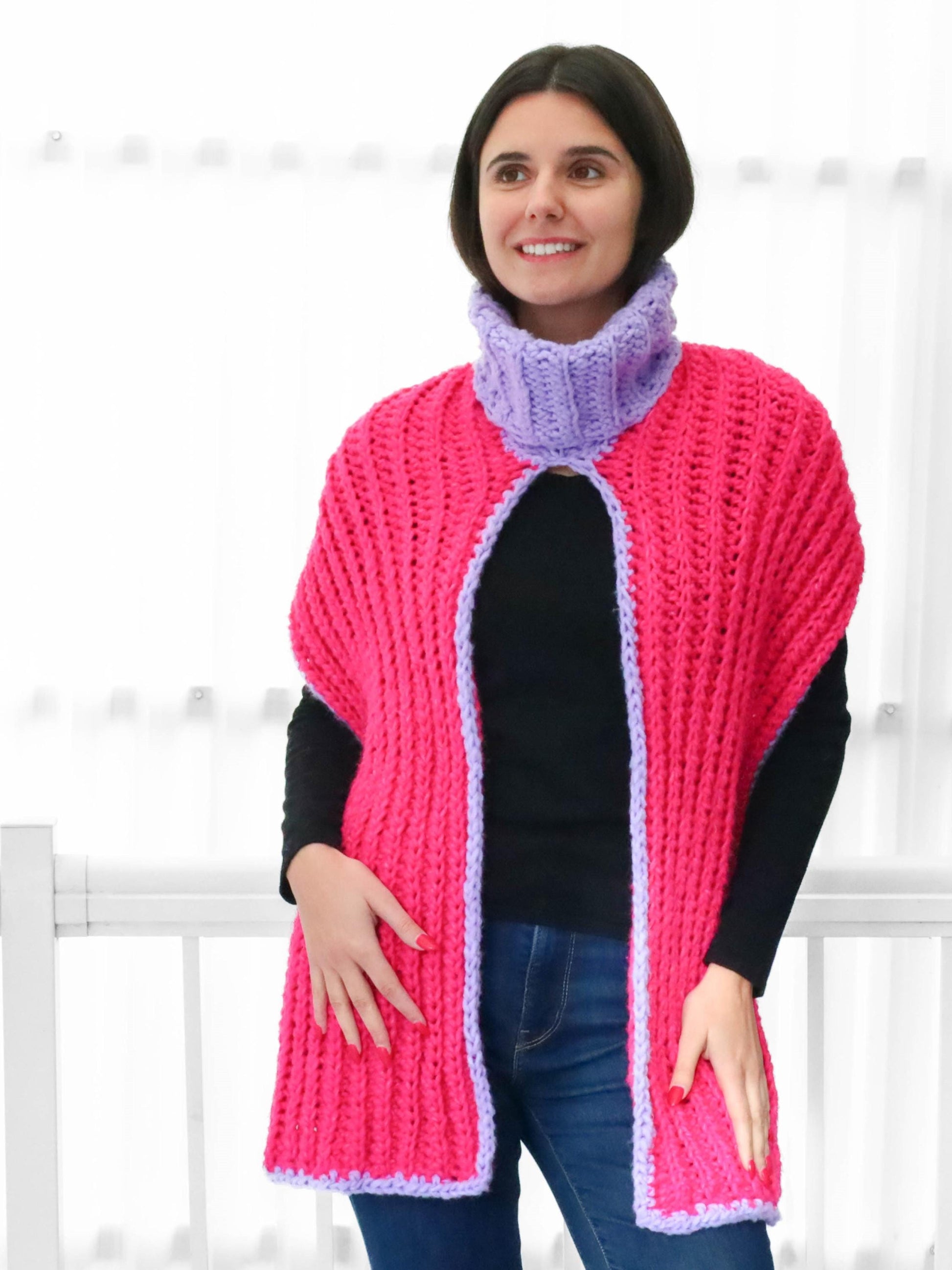 May include: A pink and purple crocheted cowl with a turtleneck. The cowl is open in the front and has a long, flowing design.