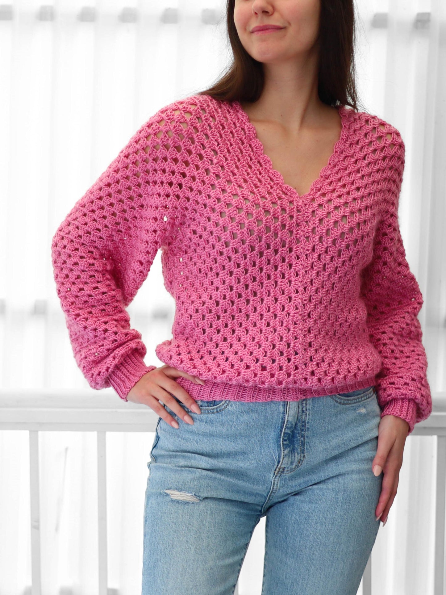 May include: A pink crocheted sweater with a v-neck and long sleeves. The sweater has a loose fit and a delicate open stitch pattern.