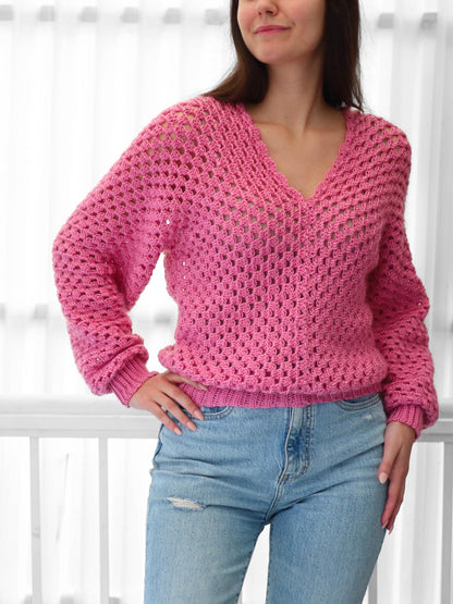 May include: A pink crocheted sweater with a v-neck and long sleeves. The sweater has a loose fit and a delicate open stitch pattern.