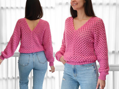 May include: A pink crocheted sweater with a deep V-neck and long sleeves. The sweater has a loose fit and a delicate openwork pattern.