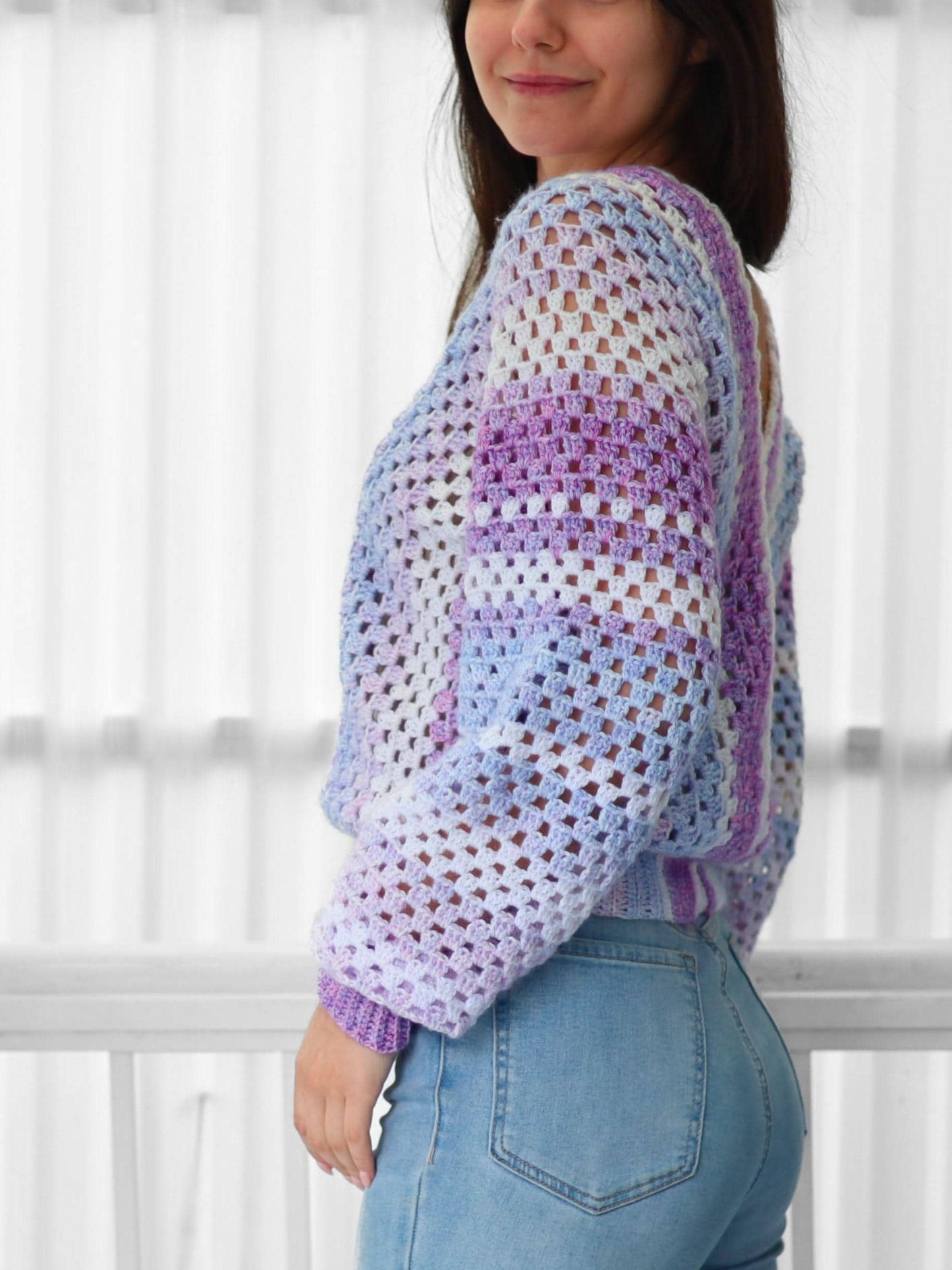 May include: A light purple, white, and blue crochet top with a loose fit and long sleeves. The top is made with a square stitch pattern.