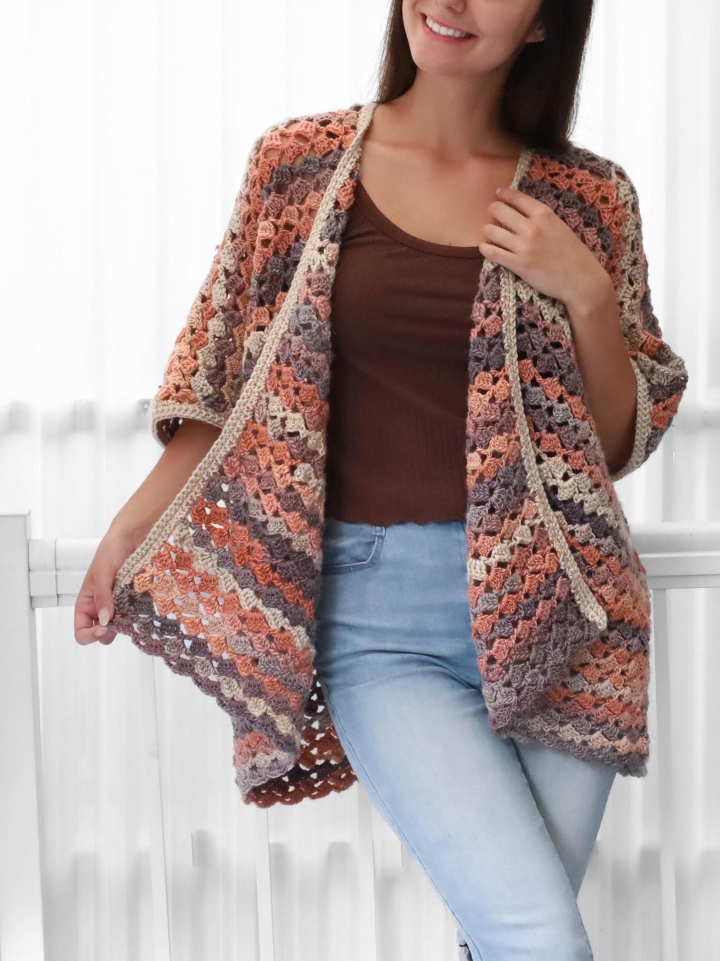 May include: A handmade crochet cardigan in shades of peach, gray, and beige. The open-front design features a geometric pattern and three-quarter sleeves. The cardigan is a cozy, stylish garment.