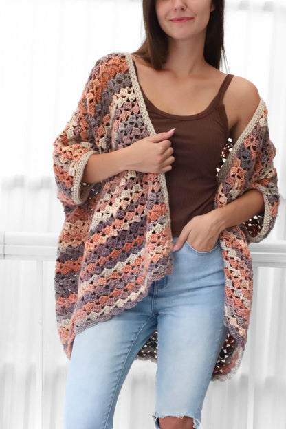May include: A handmade crochet cardigan in a mix of peach, purple, and beige tones. The open-front design features a textured stitch pattern and a neutral border. This cozy, lightweight garment is perfect for layering.