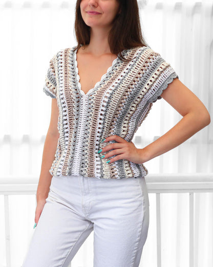May include: A short-sleeved, V-neck crochet top in a neutral color palette of white, gray, and tan. The top features a scalloped neckline and a textured, open weave design. The garment is handmade and suitable for warm weather.