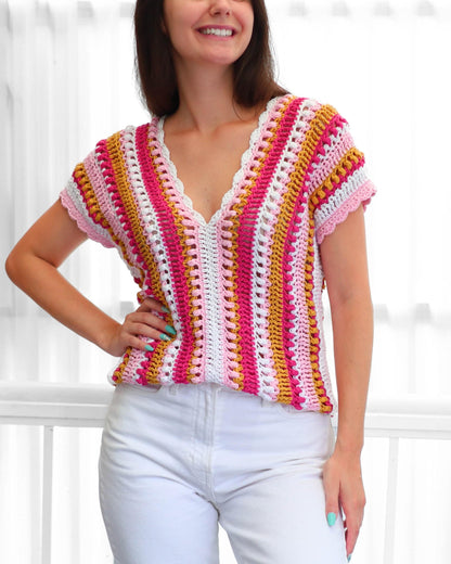 May include: A colorful, short-sleeved crochet top with a V-neck. The top features vertical stripes in shades of pink, white, yellow, and a scalloped edge. The garment is handmade and has a relaxed fit.