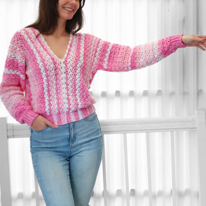 May include: A pink and white crochet sweater with a V-neck. The sweater has a striped pattern and long sleeves. The sleeves are a gradient of pink and white. The person is wearing blue jeans.